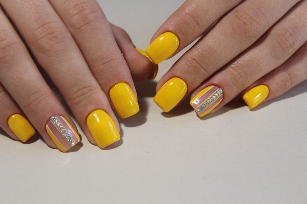 Esmalte de uñas amarillo con rayas diagonales y pedrería.