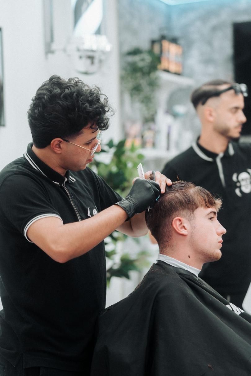 Un barbero corta el pelo a un cliente en un salón mientras otro hombre observa.