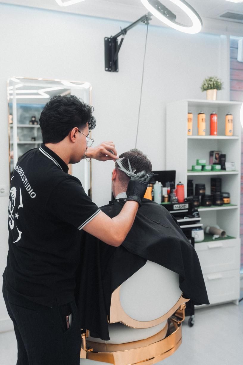 Barbero cortando el pelo en un salón bien iluminado. Lleva camisa negra, guantes y gafas. 
