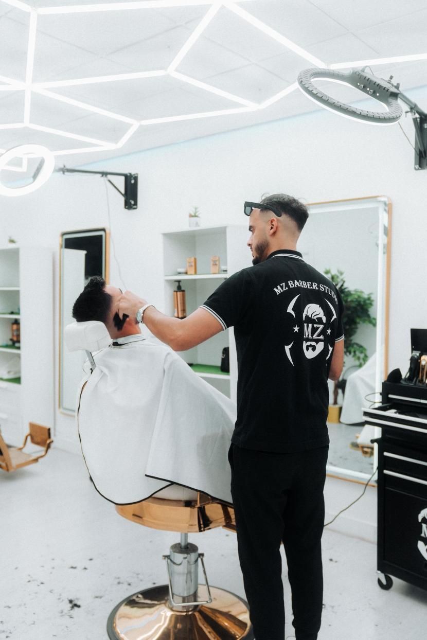 Un barbero afeita la cara de un cliente en un salón moderno con luces de neón.
