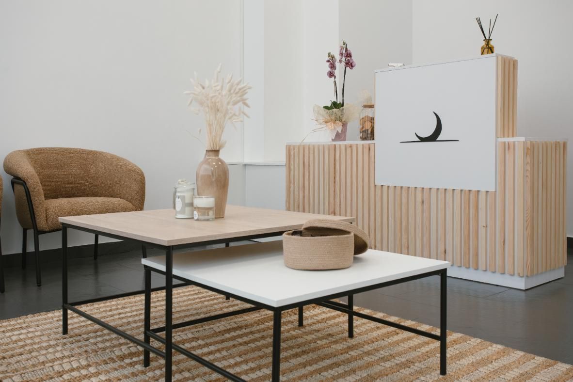 Área de recepción con un mostrador de madera clara, una mesa de café anidada, una silla mullida y un jarrón decorativo.