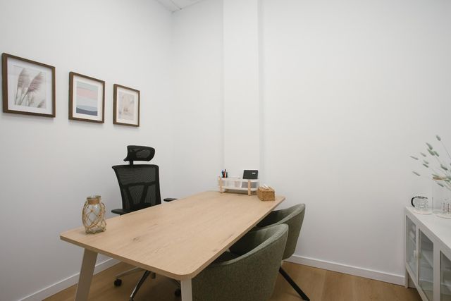 Consultorio del terapeuta: escritorio con dos sillas, sofá rosa, casita de juegos y una ventana con persianas.