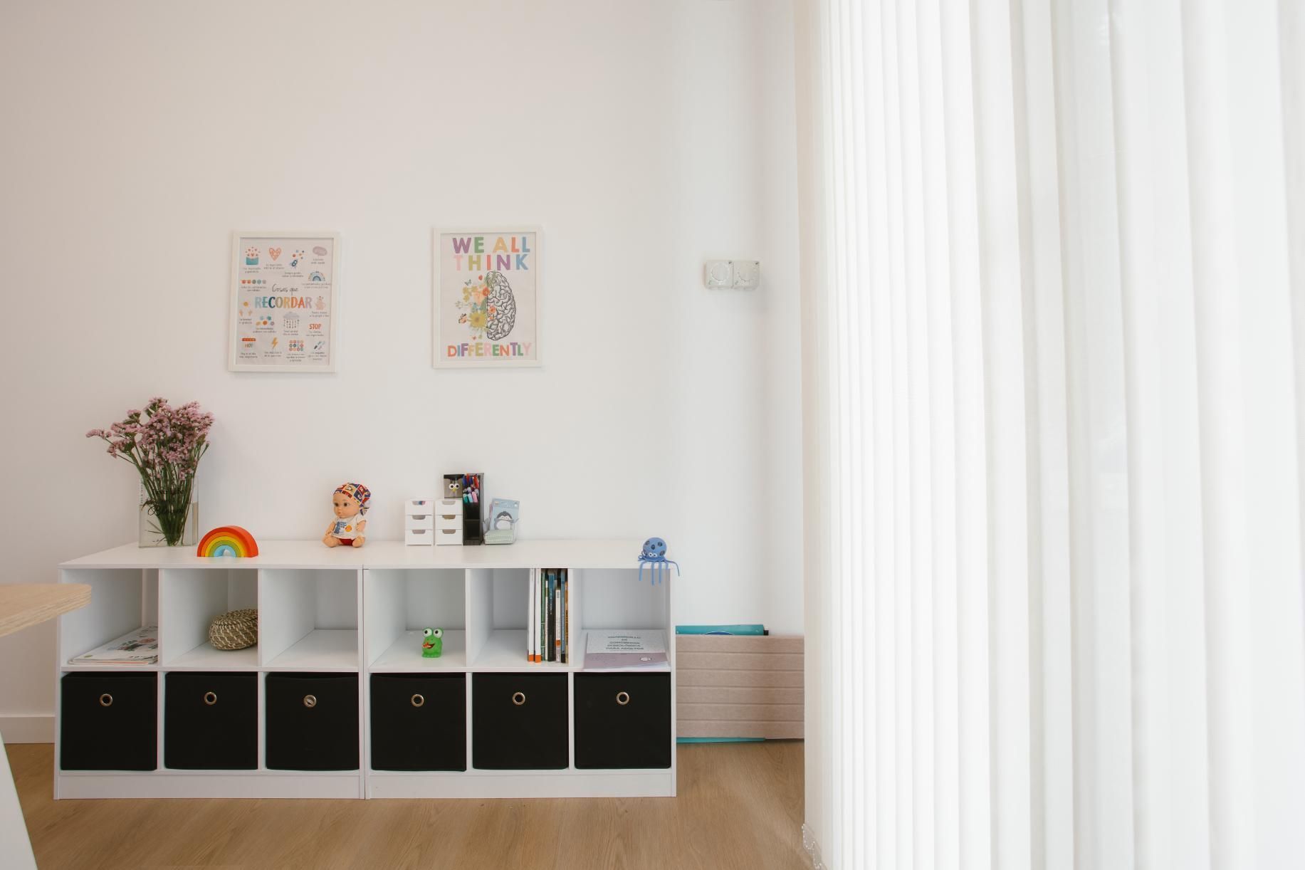 Unidad de almacenamiento blanca con decoración sobre una pared blanca y cortinas transparentes.