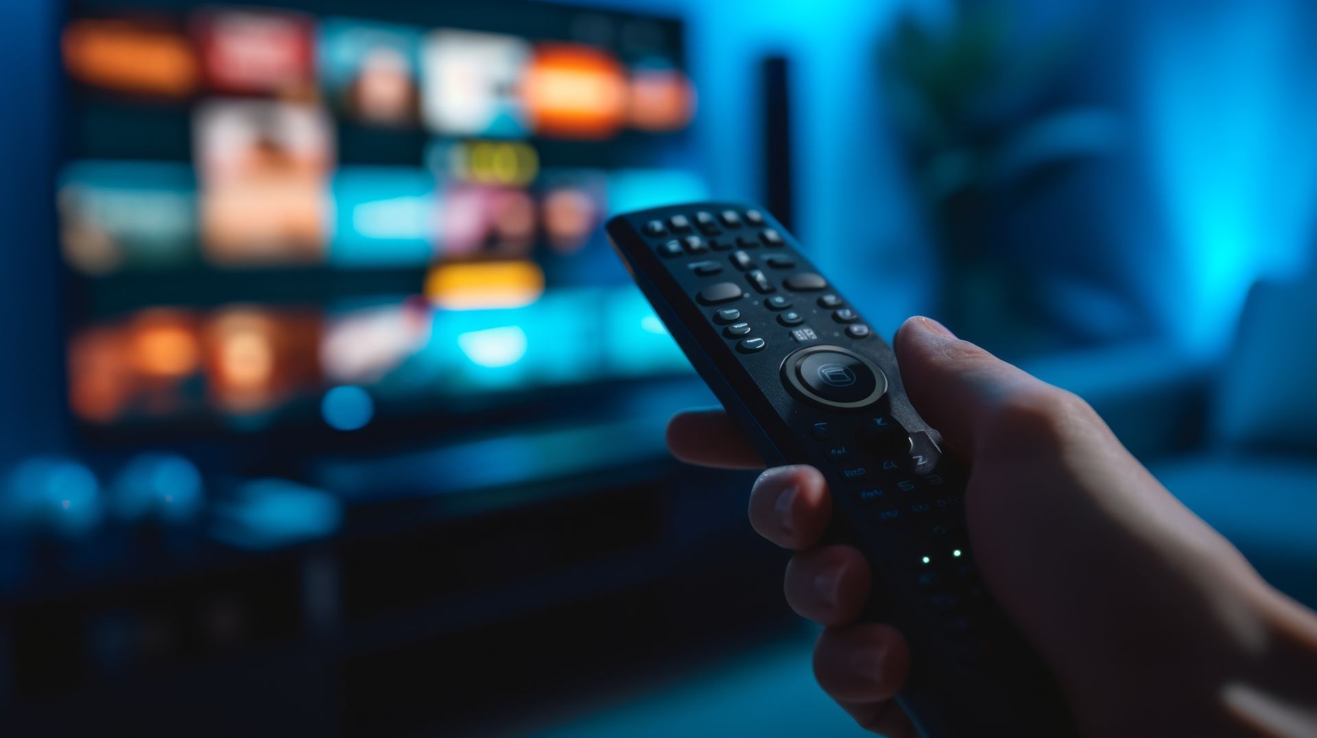 Eine Person hält eine Fernbedienung vor einem Fernseher.