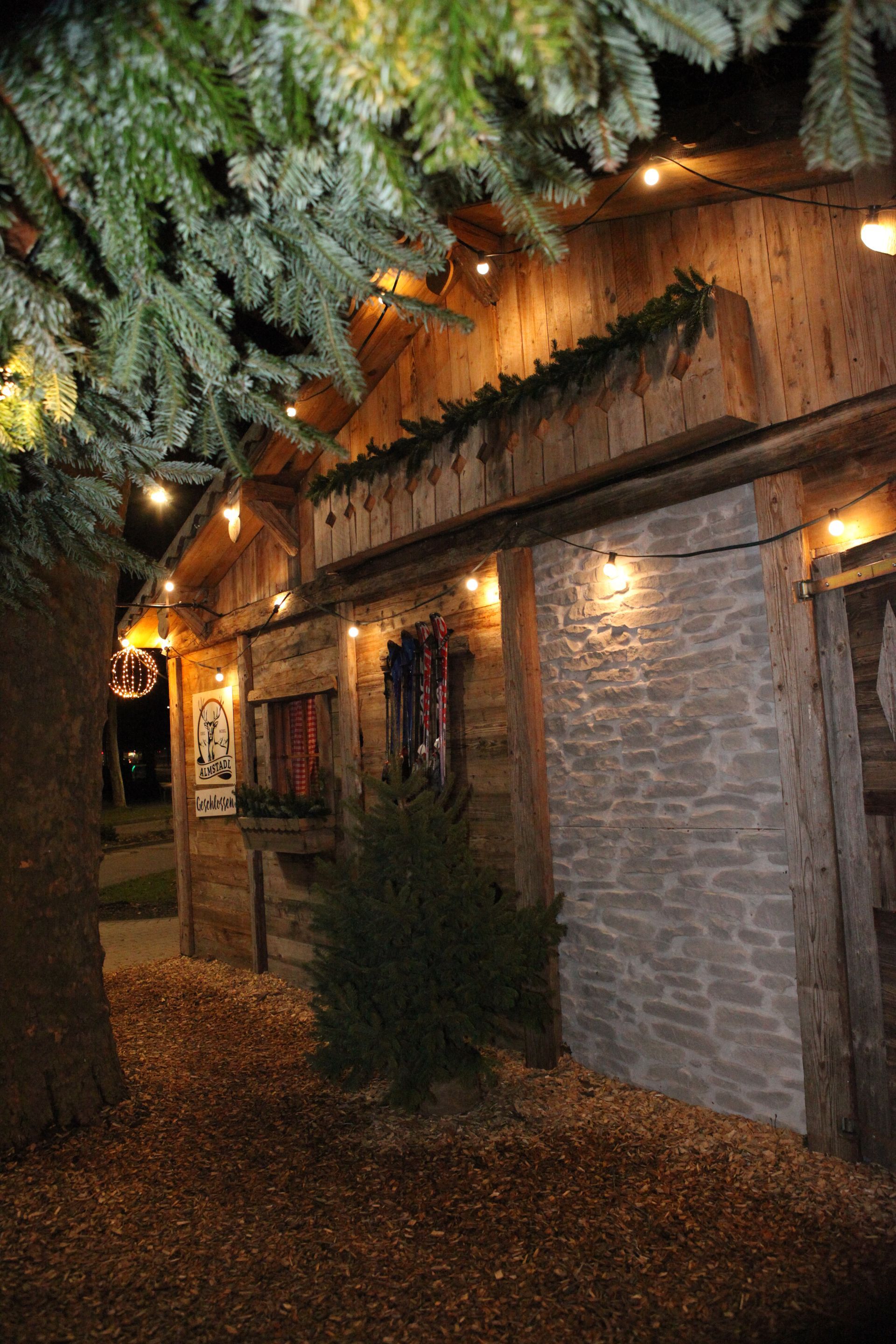 Holzgebäude mit Lichterkette und immergrünem Zweig; Winterlandschaft.