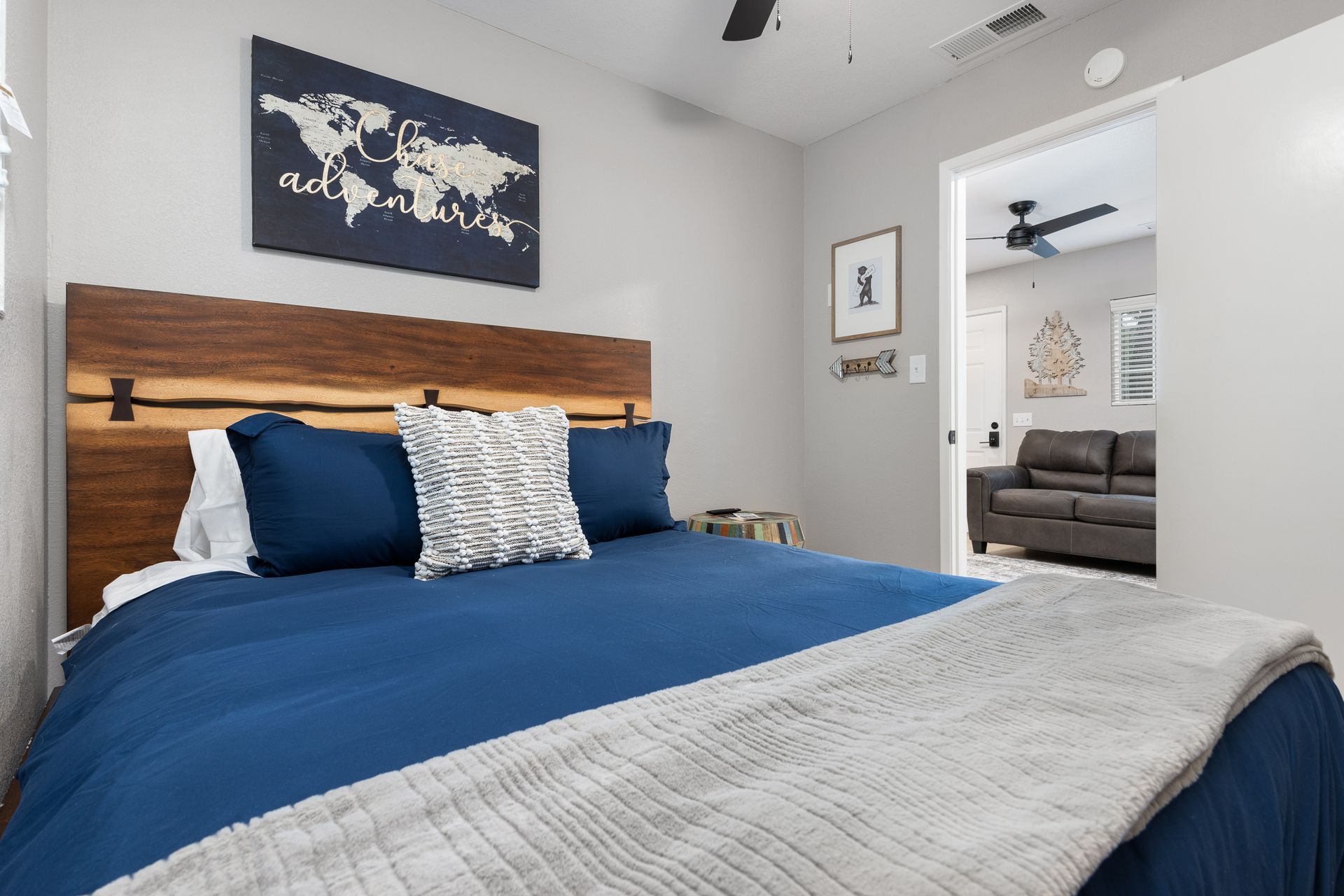 Bedroom with blue bed, wooden headboard, world map art, and doorway to a living room.