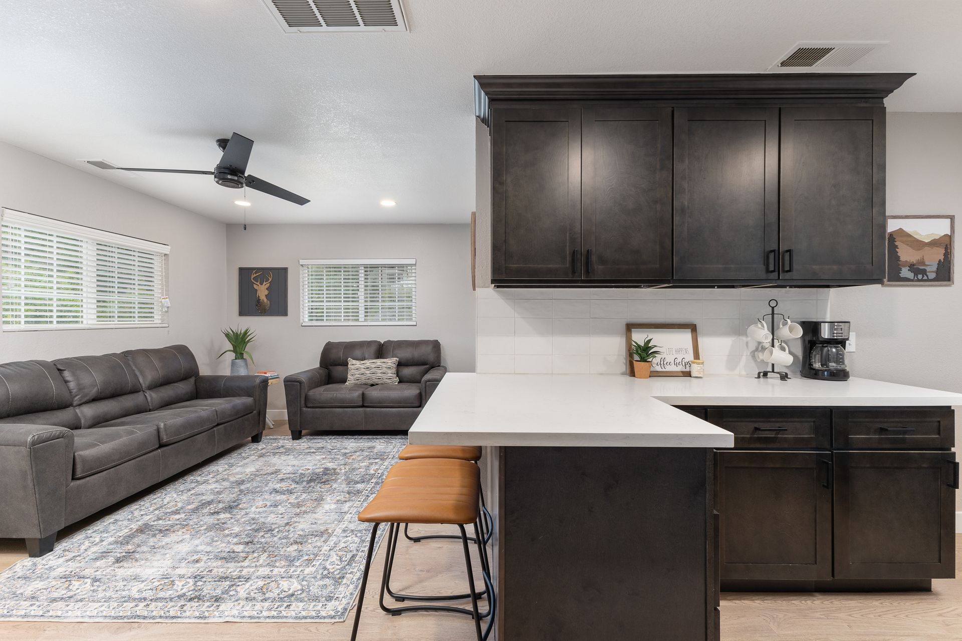 Open-concept living space. Kitchen with dark cabinets, counter with barstool, and living area with gray sofas and rug.