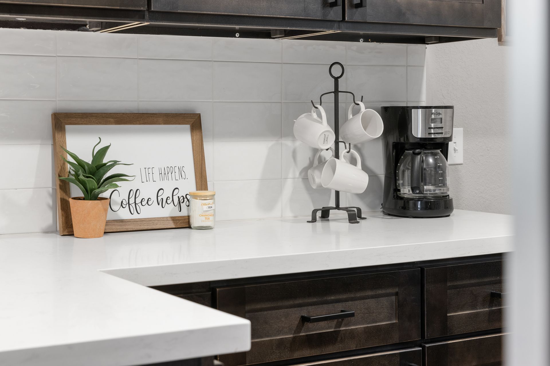 Kitchen counter with coffee maker, mug rack, and decorative sign.