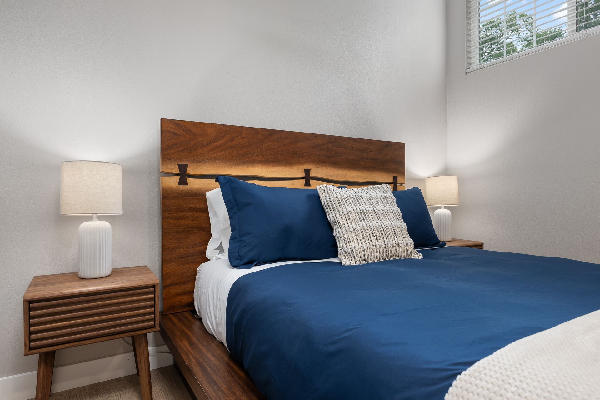 Bedroom with blue bedding, wooden headboard, and bedside tables with lamps.
