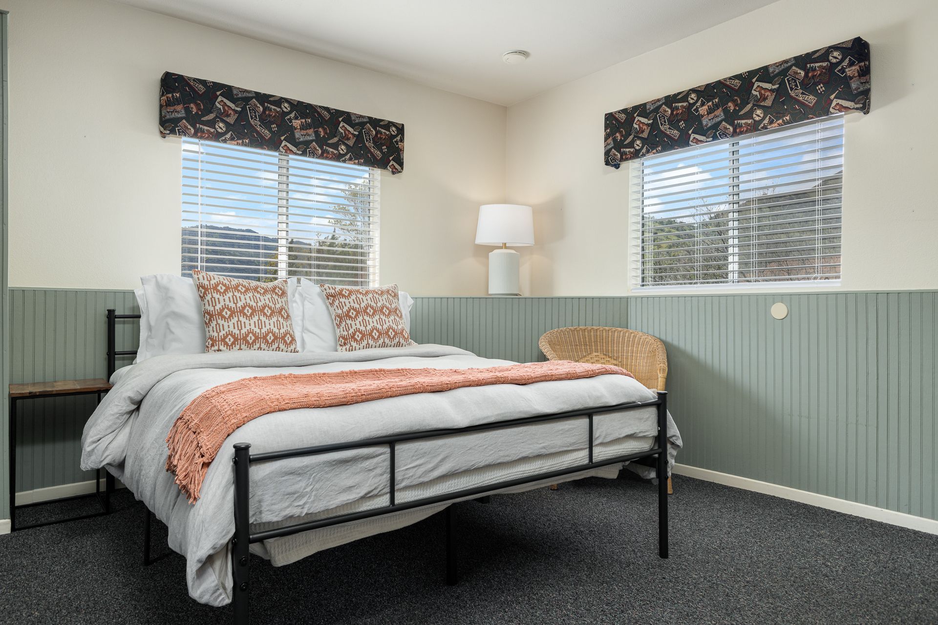 Bedroom with bed, windows, floral valances, and seafoam paneling.