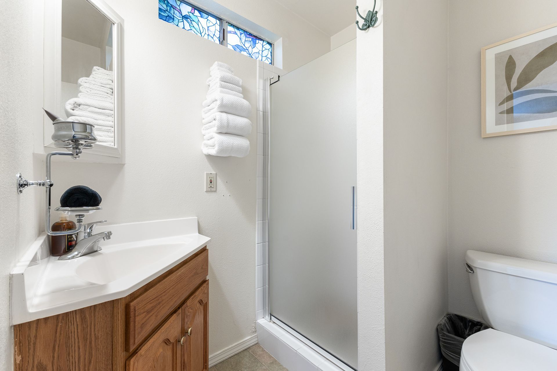 Small bathroom with a sink, shower, and toilet. White walls and towels, wood-tone cabinet.