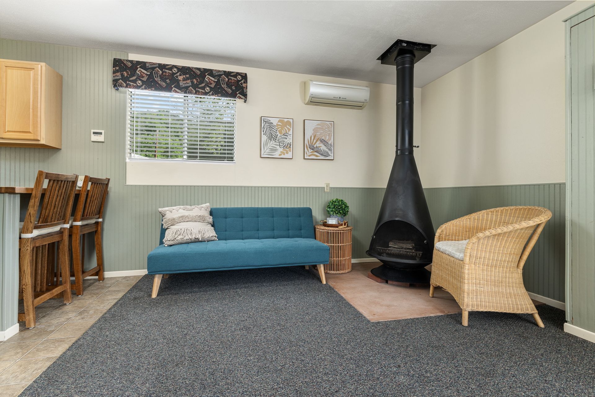A cozy living room with teal sofa, wicker chair, fireplace, and gray carpet.