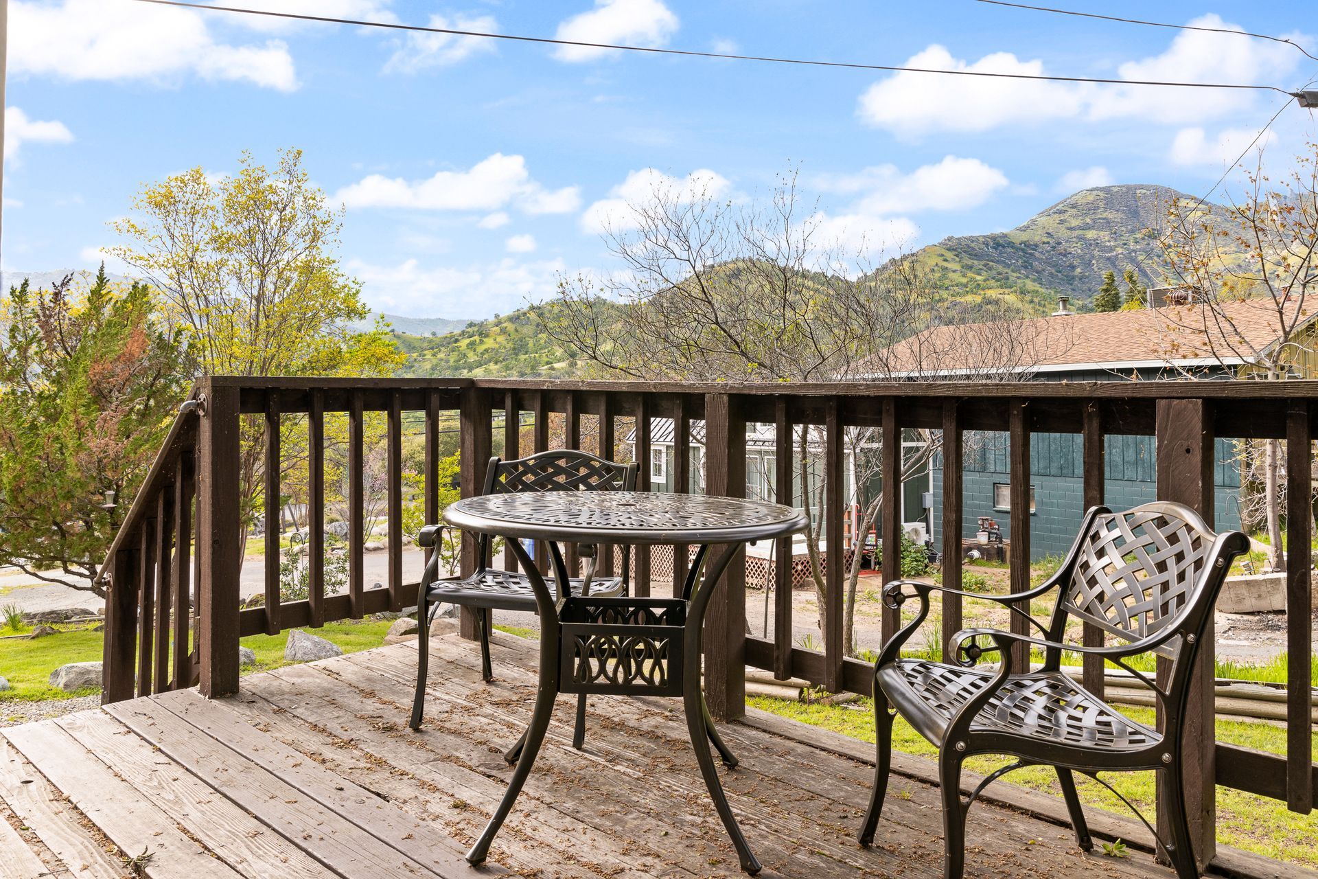 Wooden deck with table and chairs, overlooking a mountain range under a blue sky with clouds.