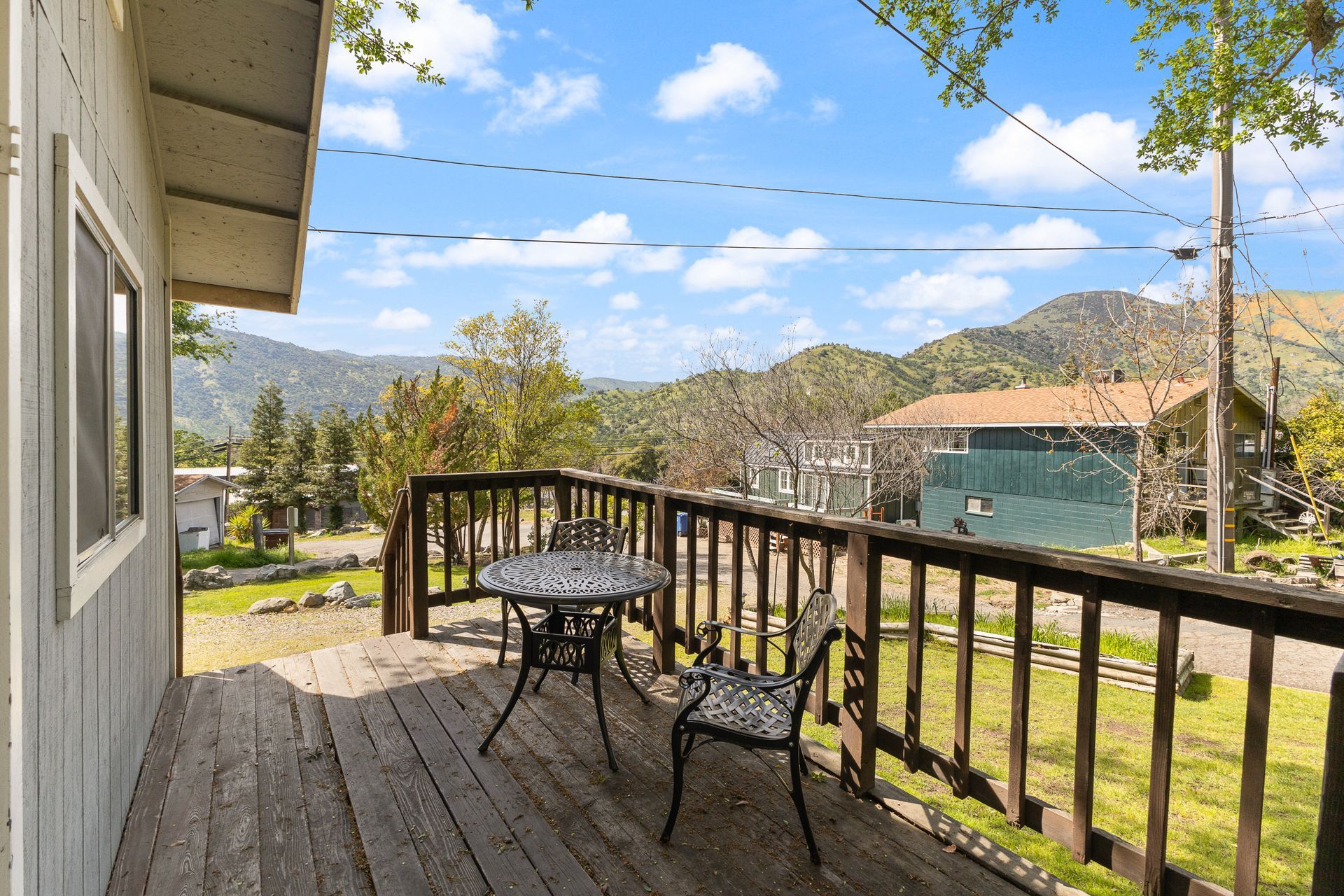 A wooden deck with table and chairs overlooks a hillside town under a blue sky.