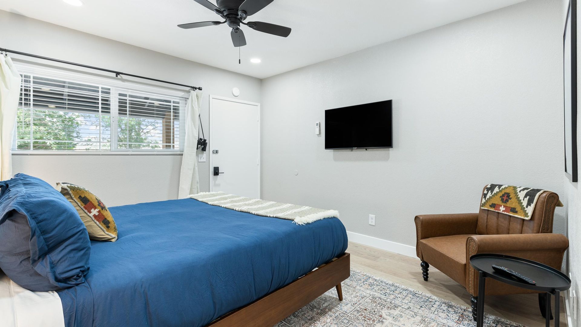 Bedroom with King bed, brown armchair, and a mounted Smart TV.