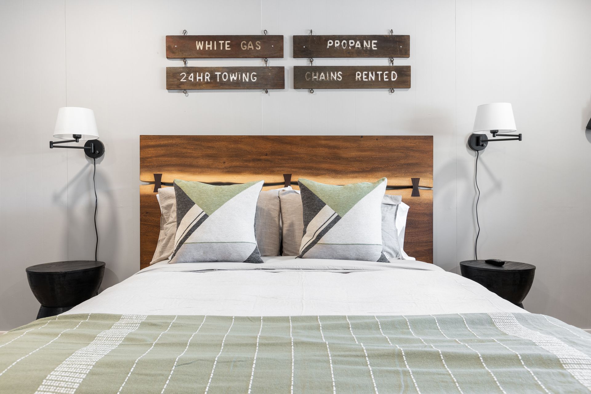 Bedroom with a bed, pillows, lamps, and art. Wooden headboard, green and white accents.