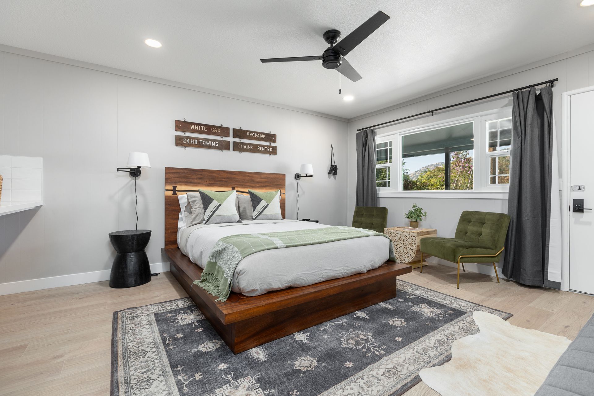 Bedroom with wooden bed, chairs, rug, and window with dark curtains; neutral colors.