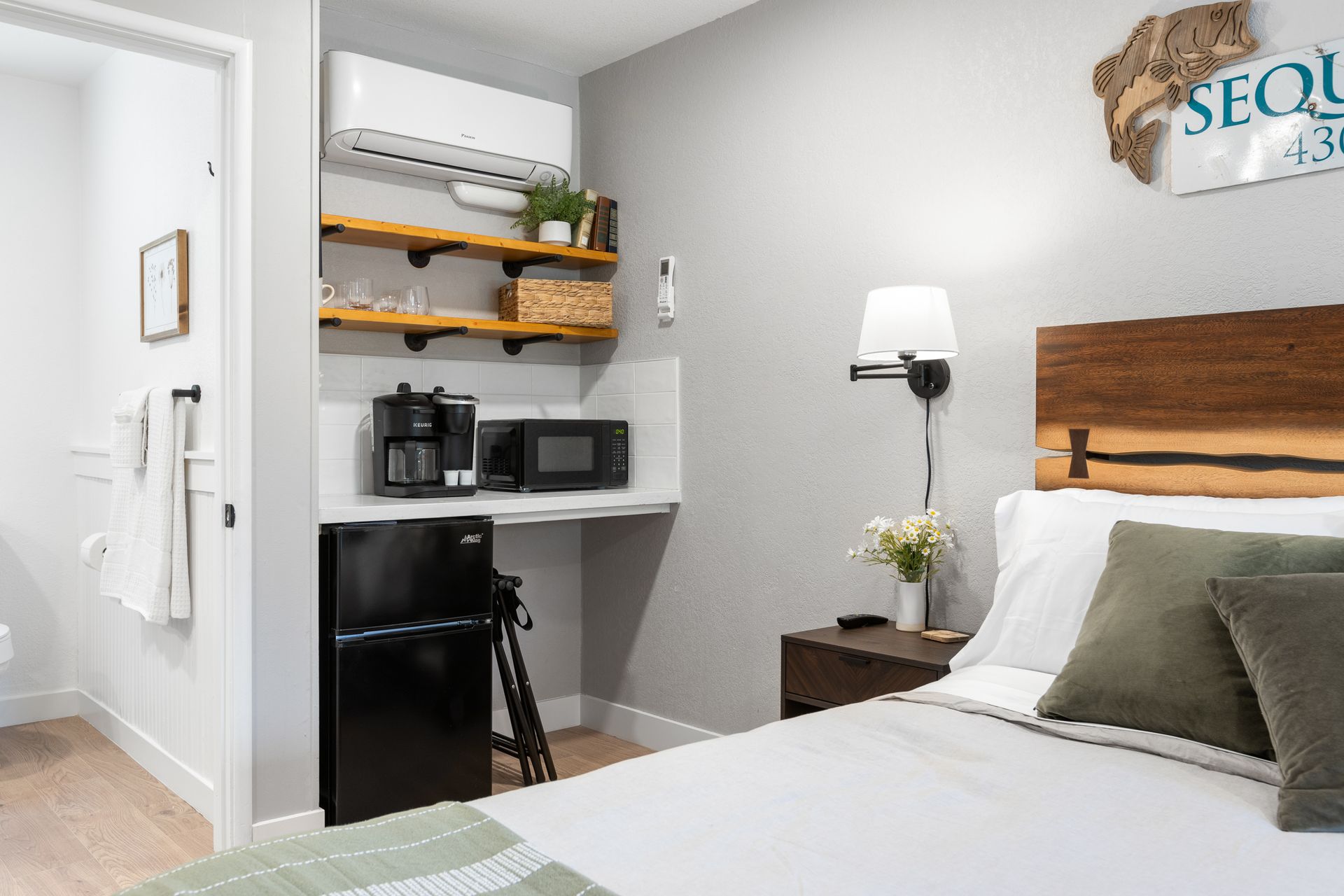 Small motel room with a bed, mini-fridge, microwave, coffee maker, and shelves.