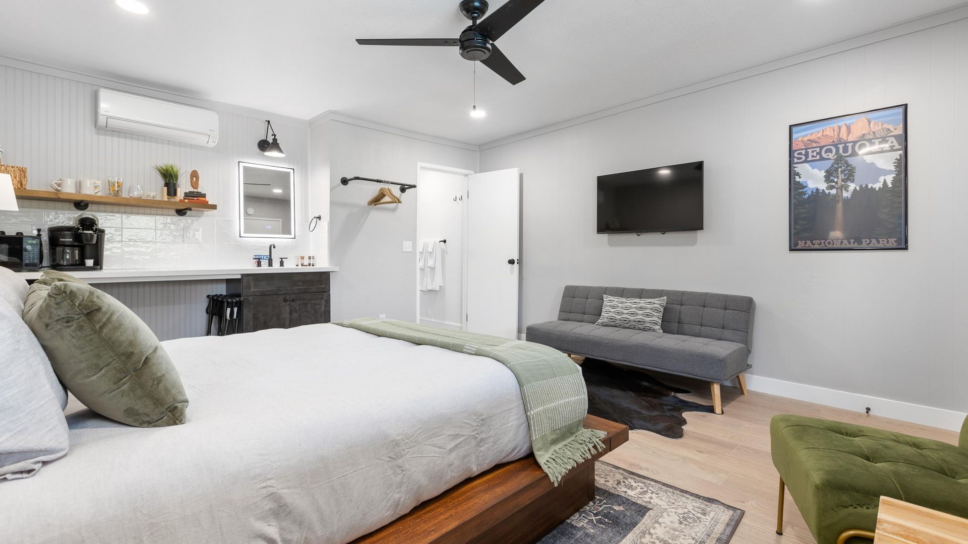 Bedroom with king bed, gray sofa, green chair, and a wall-mounted TV.