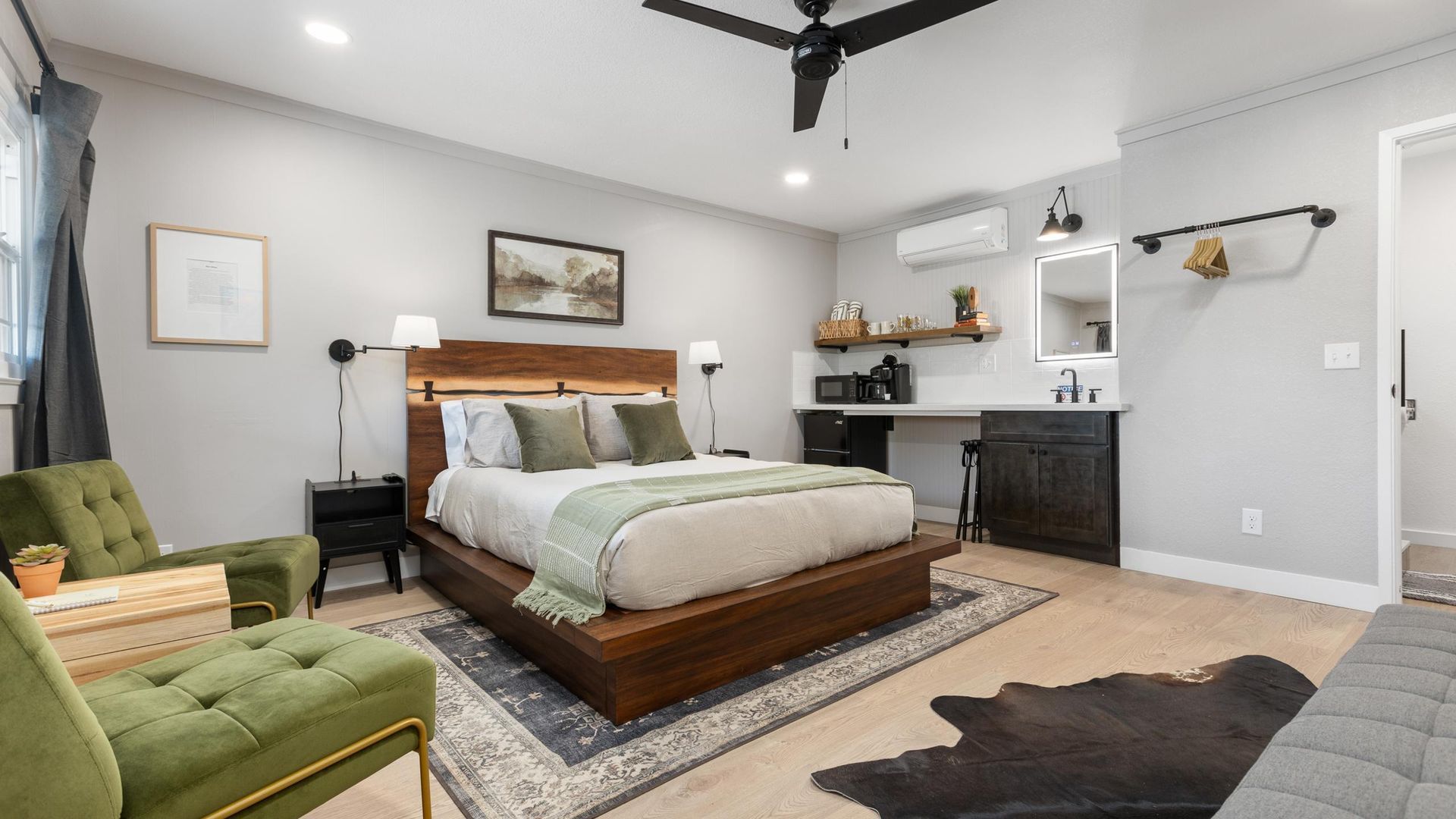 Bedroom with bed, green chairs, desk, and rug. Neutral walls, dark furniture, and a rustic feel.