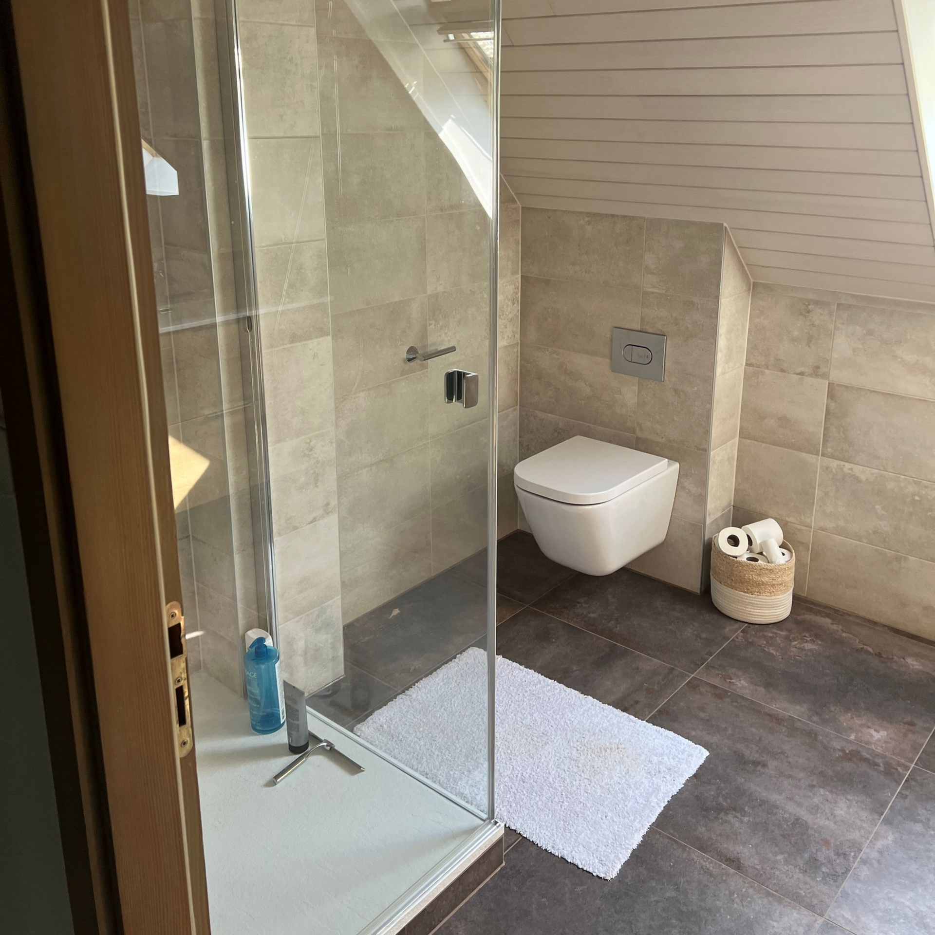 Salle de bains avec douche en verre, toilettes et carrelage beige.