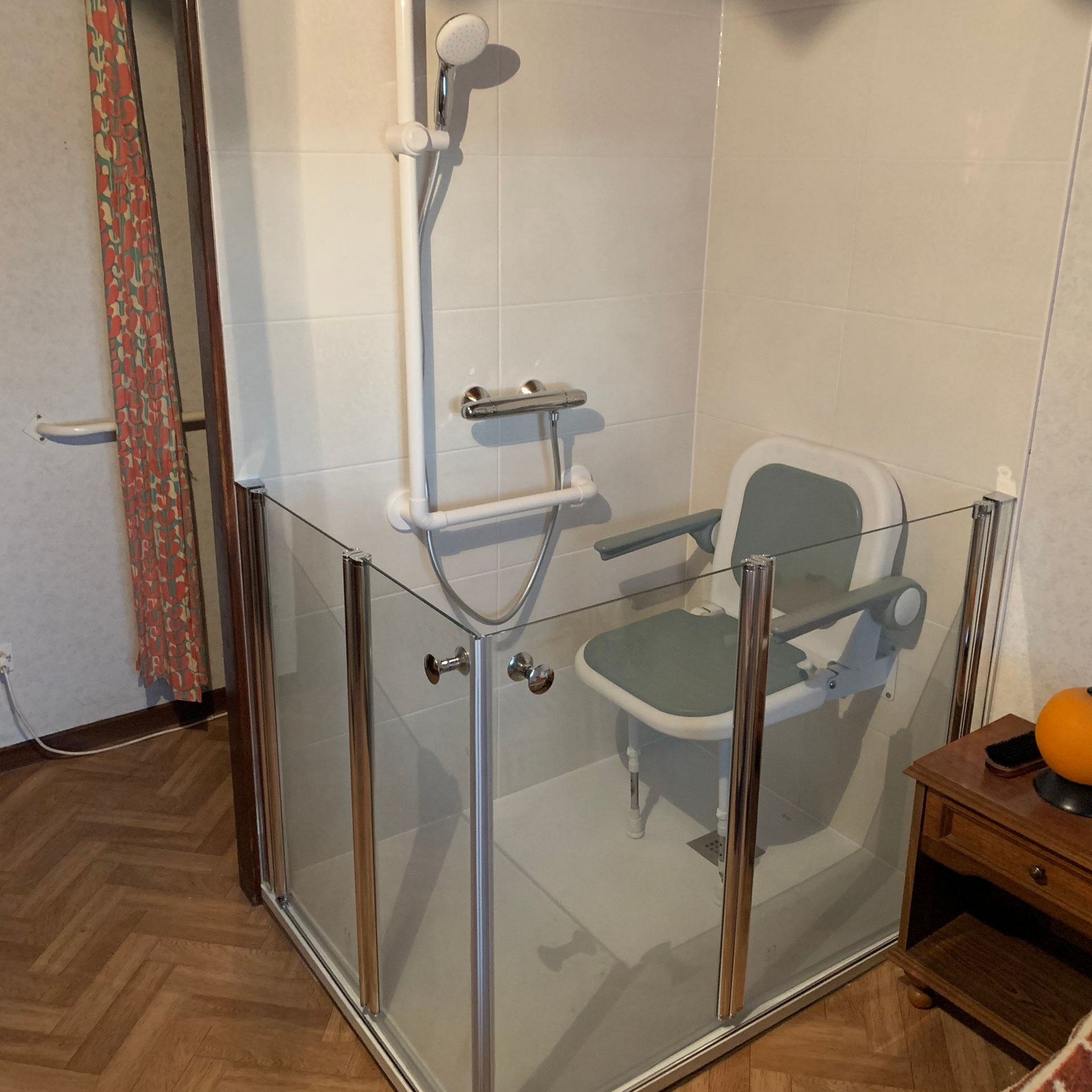 Cabine de douche accessible avec siège rabattable et portes en verre dans une salle de bains.