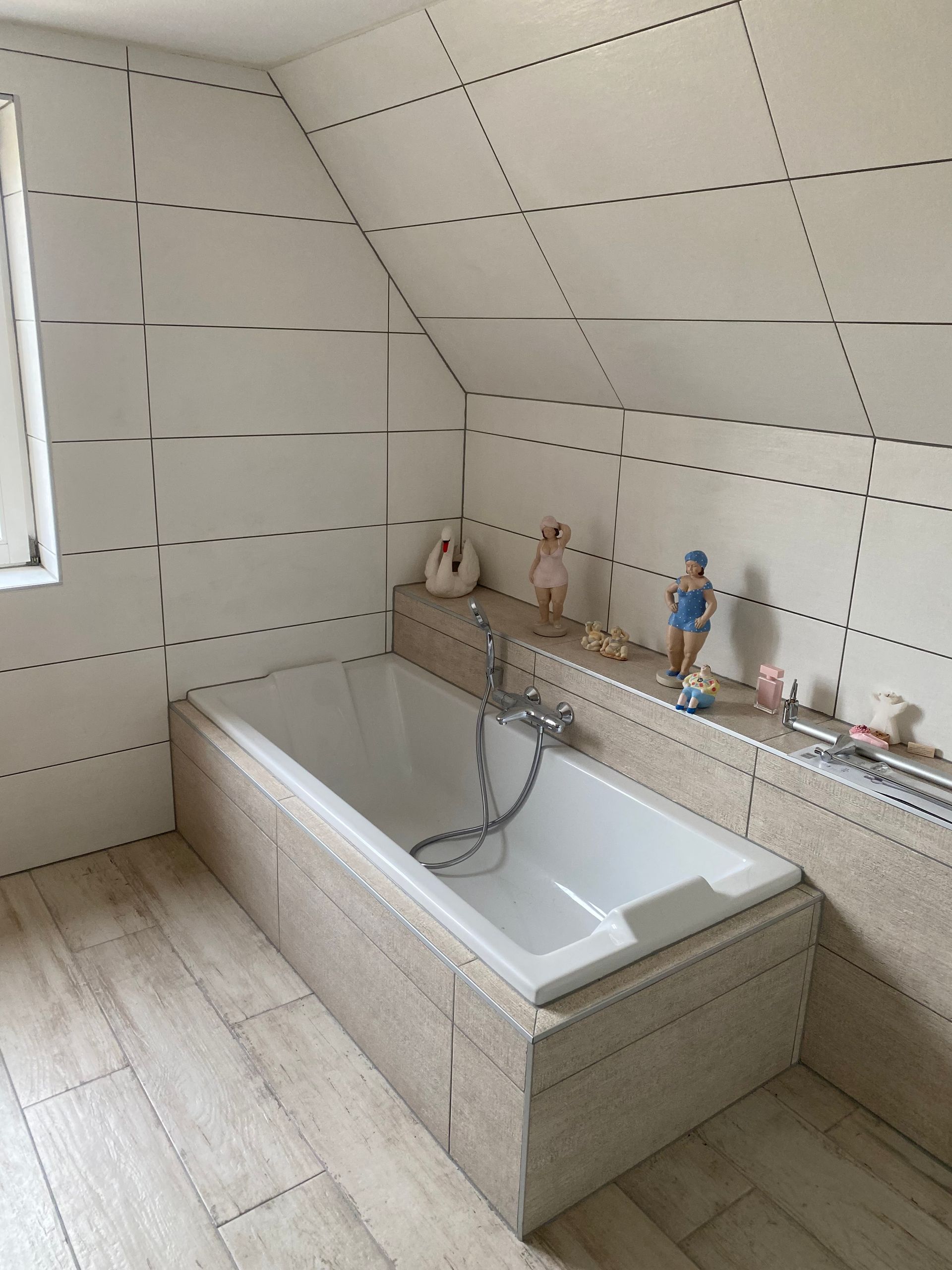 Salle de bains avec baignoire blanche, murs carrelés clairs et parquet.