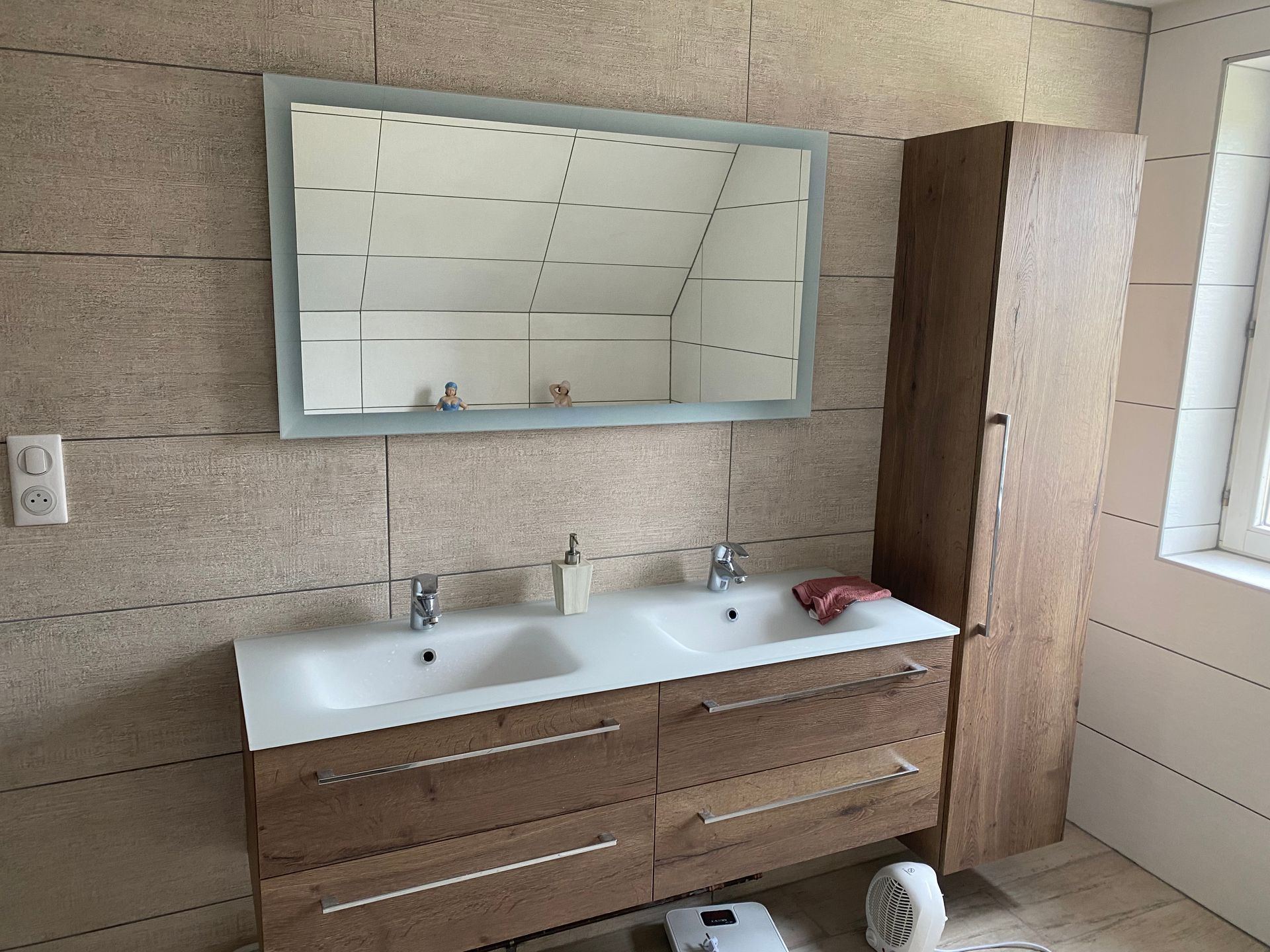 Salle de bains avec meuble lavabo à double vasque, miroir, armoire haute et murs carrelés de couleur claire.