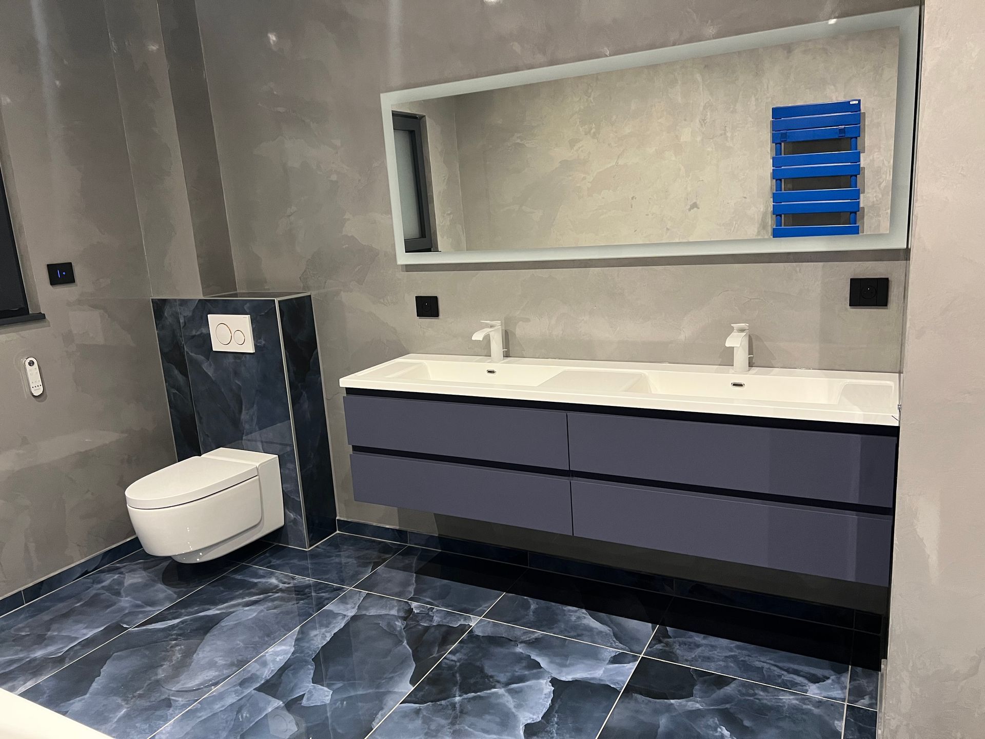 Salle de bains moderne avec meuble double vasque suspendu, grand miroir et toilettes suspendues.