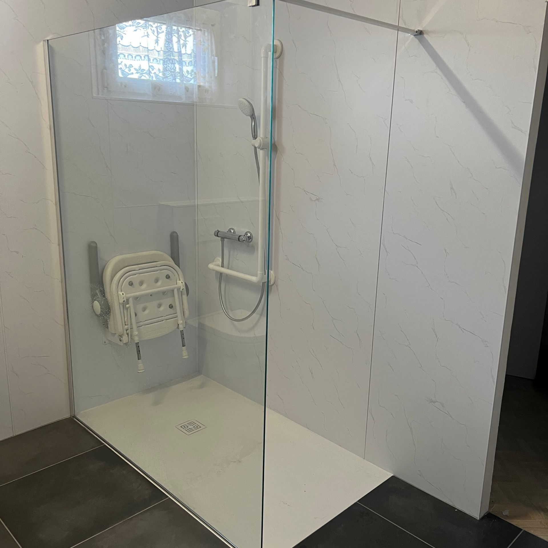 Douche accessible avec siège rabattable, barre d'appui et porte en verre.
