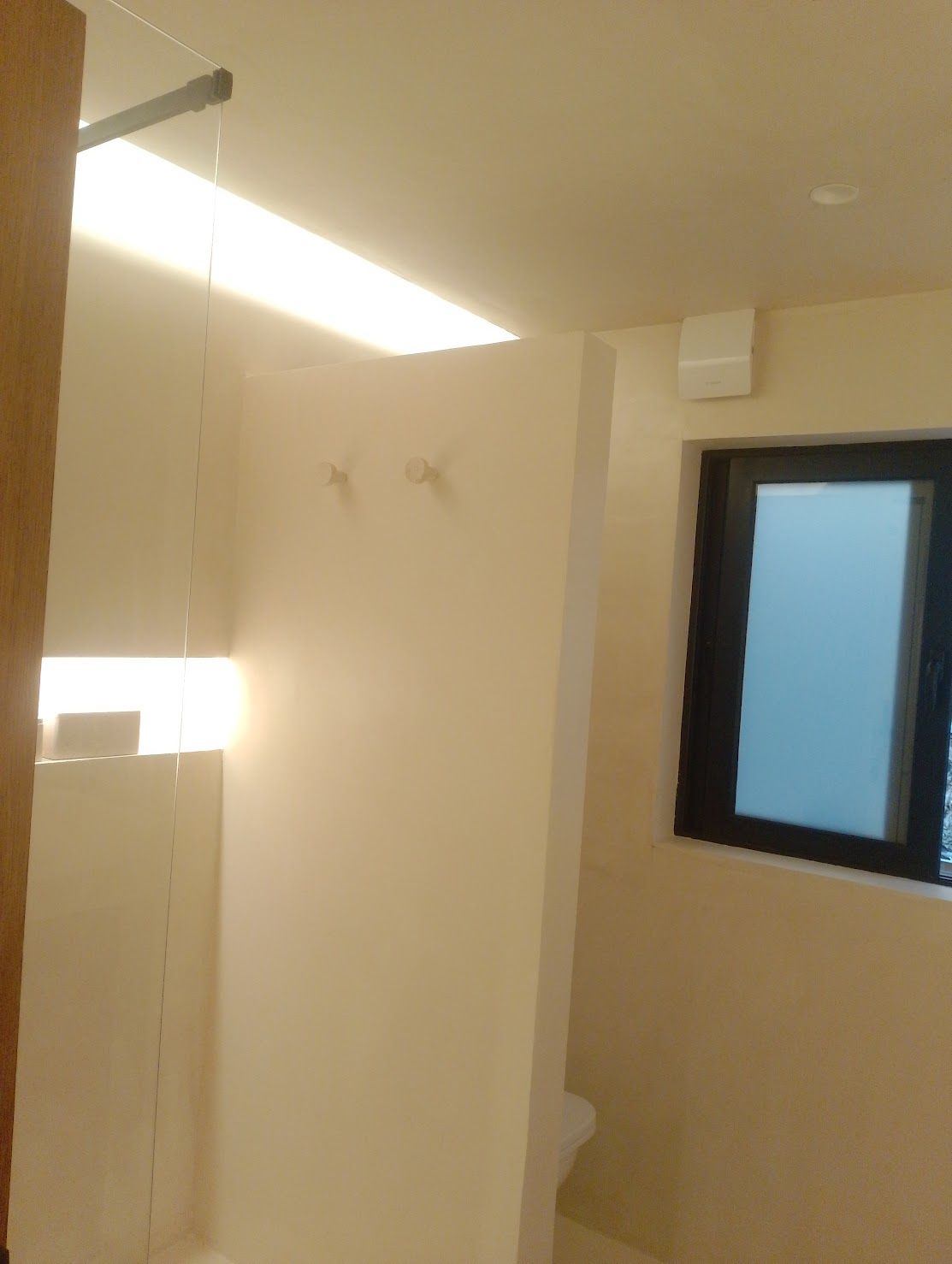 Un baño con paredes blancas y una ventana negra.