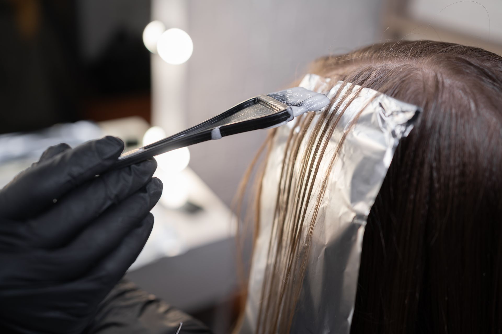 Eine Stylistin trägt mit einem Pinsel Haarfarbe auf in Folie gewickelte Strähnen auf. Nahaufnahme im Salon.