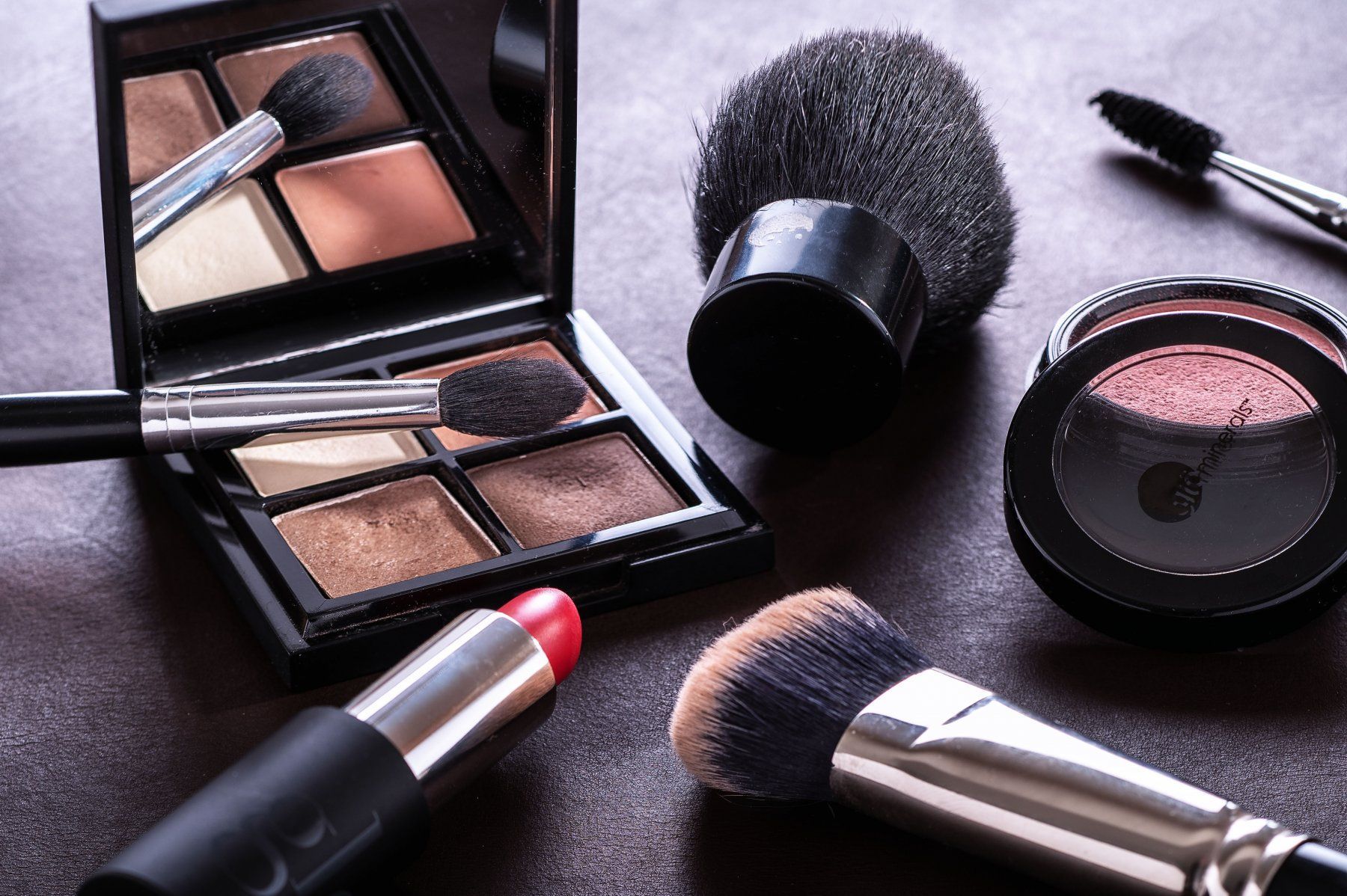 Make-up-Produkte wie Lidschatten, Pinsel, Lippenstift und Rouge auf dunklem Untergrund.