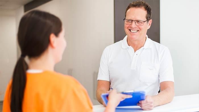 Ein Mann spricht mit einer Frau an einem Empfangstresen in einem Krankenhaus.
