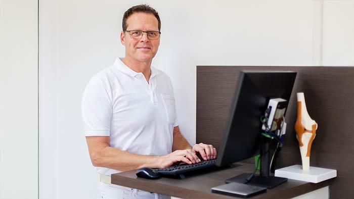 Ein Mann steht an einem Schreibtisch und tippt auf einem Computer.