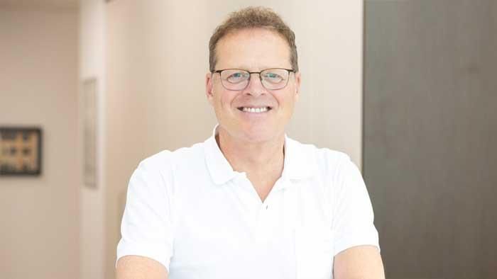 Ein Mann mit Brille und weißem Hemd lächelt in die Kamera.