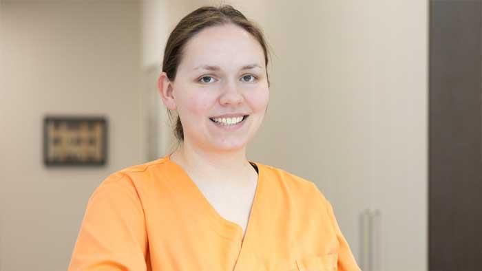 Eine Frau in einem orangefarbenen OP-Kittel lächelt in die Kamera.