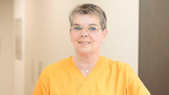 Eine Frau mit Brille und orangefarbenem Kasack lächelt in die Kamera.