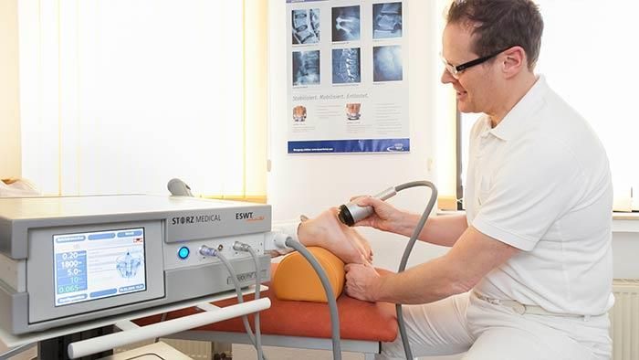 Ein Mann behandelt den Fuß eines Patienten mit einer Maschine