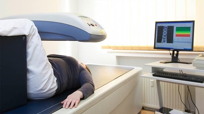 Eine Frau liegt auf einer Maschine, im Hintergrund ist ein Computermonitor zu sehen.