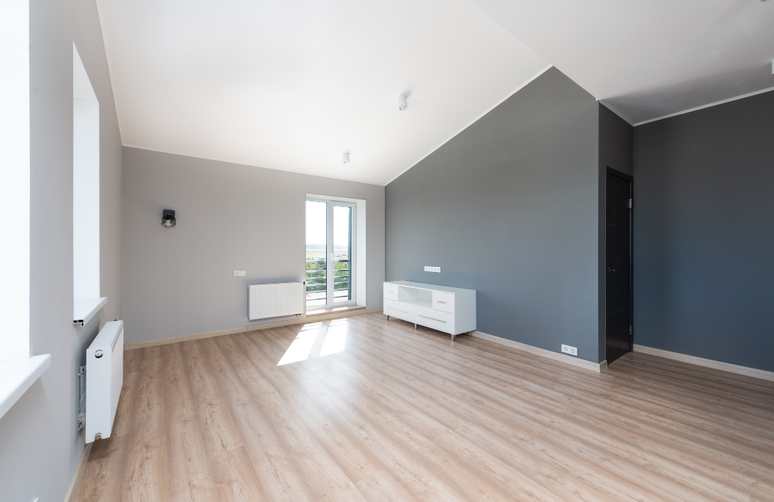 Un salon vide avec du parquet et des murs gris.