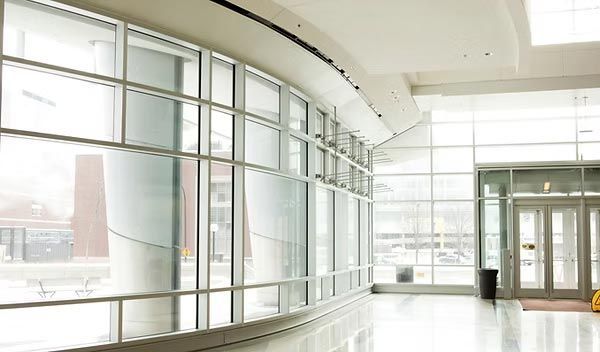 Interior de edificio moderno con grandes ventanales curvos de cristal, pilares de soporte blancos y puertas de entrada de cristal.