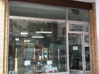La fachada de cristal de una tienda, con una exposición visible de artículos y letreros en el interior, enmarcada por pilares con textura de ladrillo.