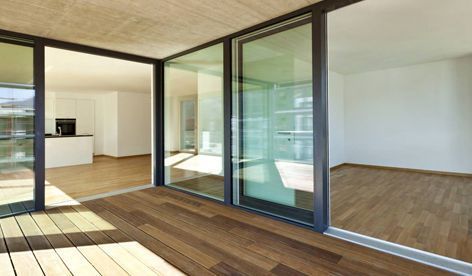 Interior moderno con grandes puertas corredizas de vidrio que dan a un patio con terraza de madera y vistas a una cocina minimalista.
