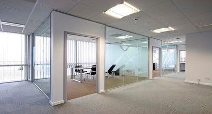 Espacio de oficinas moderno con salas de reuniones con paredes de cristal y moqueta en tonos neutros bajo una iluminación brillante en el techo.