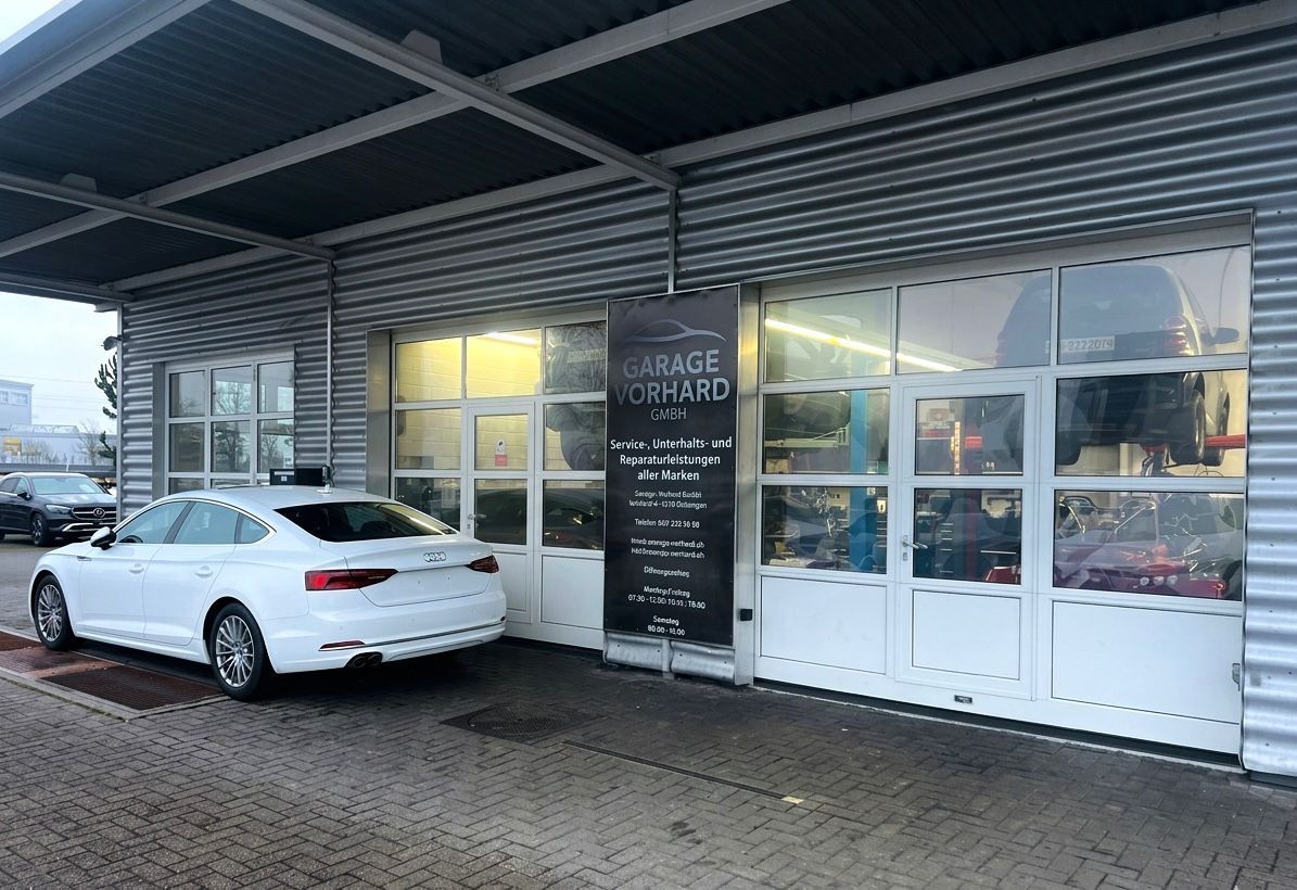 Innenansicht einer Reifenservicestation mit Reifenmontiermaschine, Radwuchtmaschine, an der Wand montierter Luftschlauchtrommel und Werkzeugen auf einem Wagen.