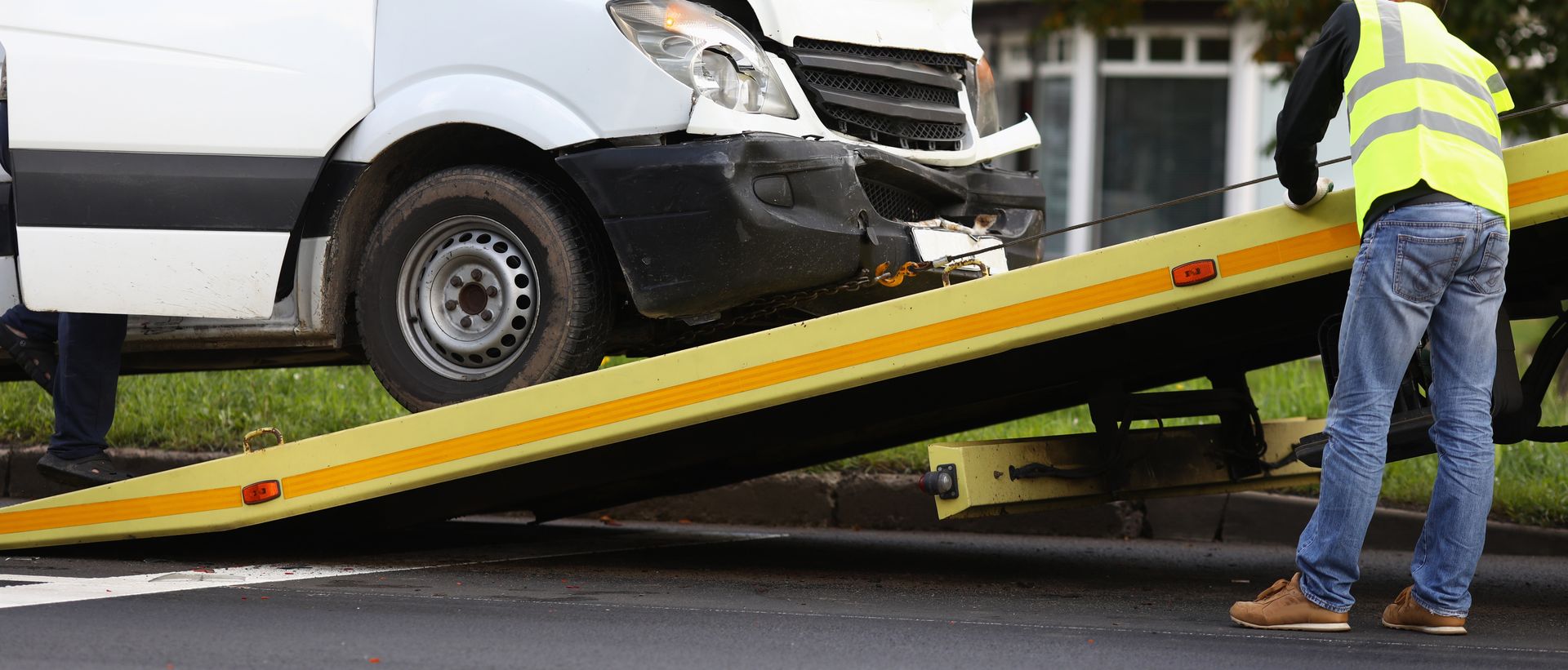 Eine Person in einer Warnweste benutzt einen Tieflader-Abschleppwagen, um einen beschädigten weissen Lieferwagen aufzuladen.