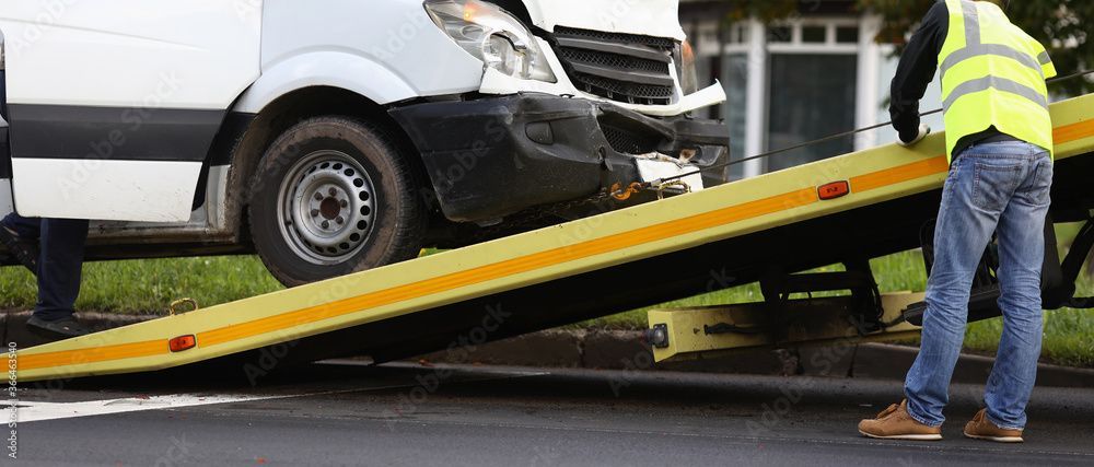 Eine Person in einer Warnweste benutzt einen Tieflader-Abschleppwagen, um einen beschädigten weissen Lieferwagen aufzuladen.