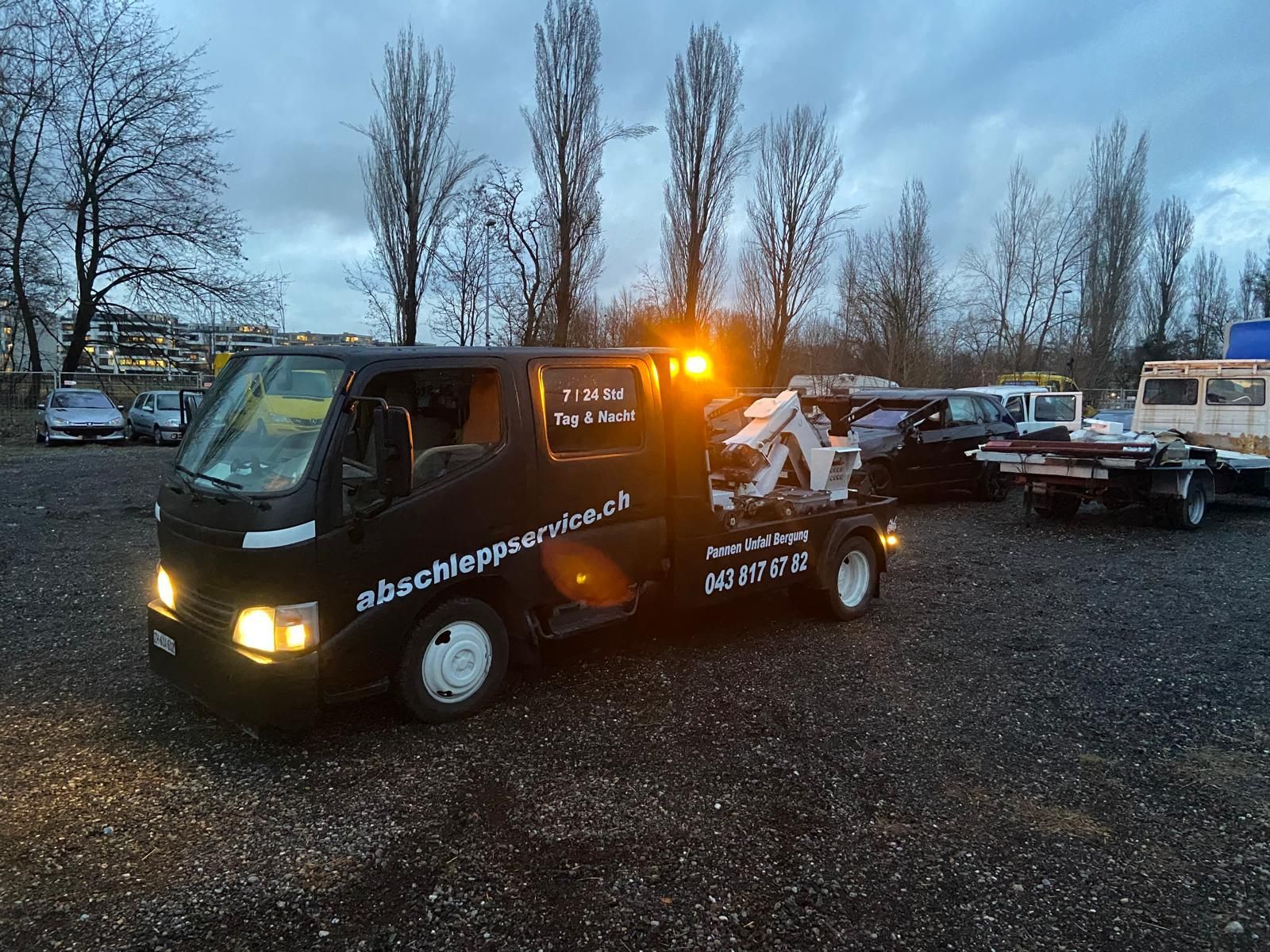 Eine Person in einer Warnweste benutzt einen Tieflader-Abschleppwagen, um einen beschädigten weissen Lieferwagen aufzuladen.