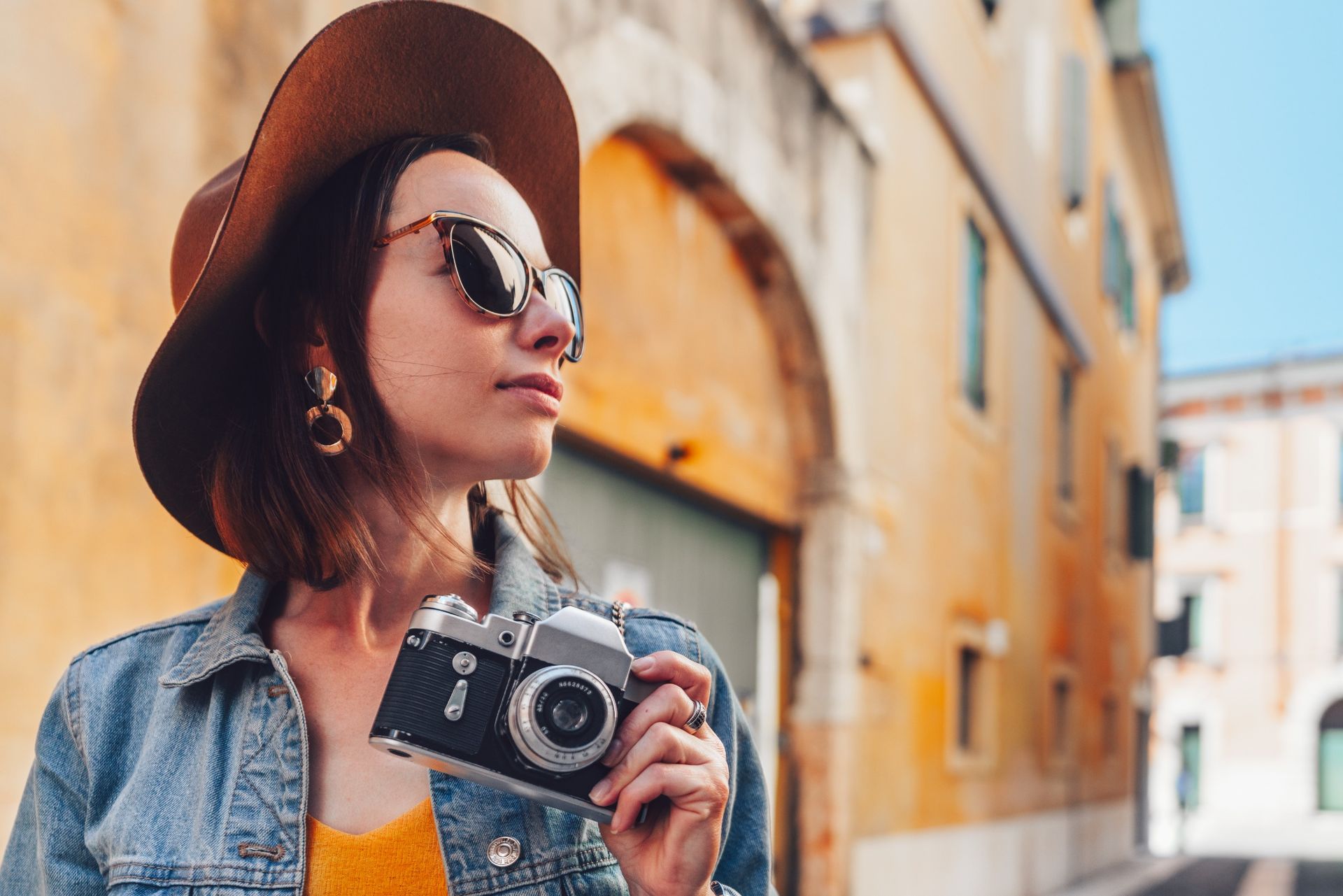 Una mujer con sombrero y gafas de sol sostiene una cámara.